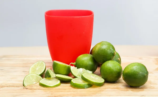 Rotes Plastikglas mit grünen Limetten drumherum — Stockfoto