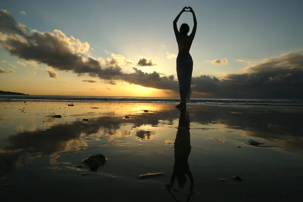 Silhouette d'une jeune femme créant la forme d'un cœur avec ses mains sur fond de coucher de soleil — Photo