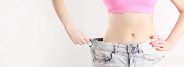 Studio shot of a young caucasian fit female wearing big jeans after diet — Stock Photo, Image