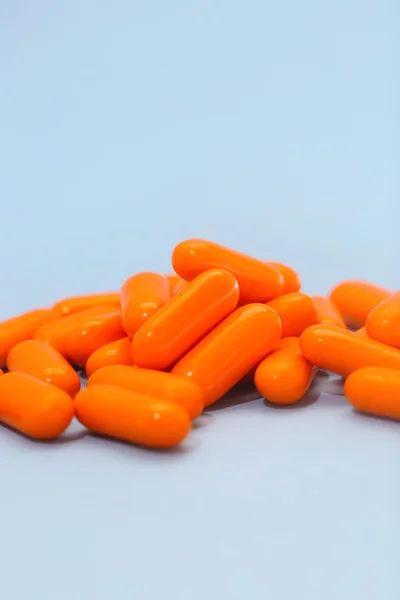 Pilha laranja de pílulas no fundo azul — Fotografia de Stock