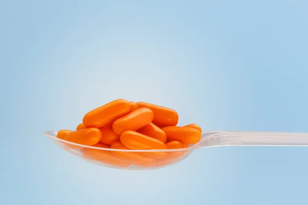 Orange pile of pills in the plastic spoon on the gradient blue background — Stock Photo, Image