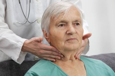 Doctor examining senior woman's thyroid glands or tonsils. clipart