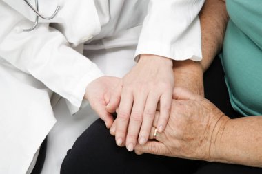 Dost canlısı bir doktor, tıbbi muayeneden sonra hastaları cesaretlendirmek, empati kurmak ve destek vermek için elini tutuyor. Güven ve tıbbi etik kavramı. 