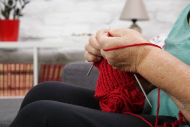 Kanepede oturan ve kırmızı yünle örgü ören son sınıf öğrencisi kadın. El yapımı yün. Yapı ve DIY kavramı.