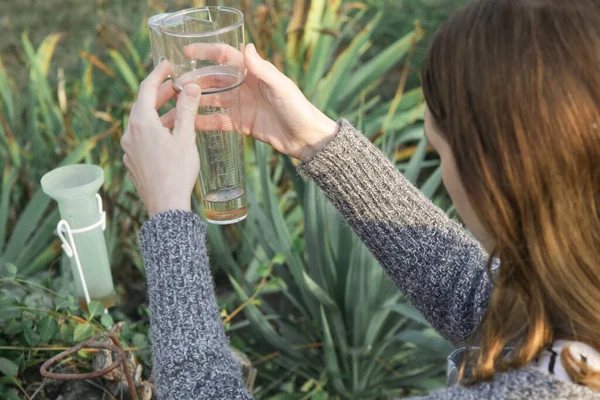 Young woman checking a rain gauge in a garden to keep track of precipitation and irrigation output.