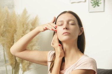 Evde yaşlanma karşıtı yüz kaldırma masajı yapan genç bir kadın. Ev kaplıcası ve cilt bakımı kavramı. 