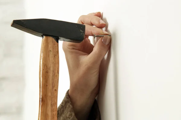 Young woman hammering nail into wall. Home improvement, DIY concept.