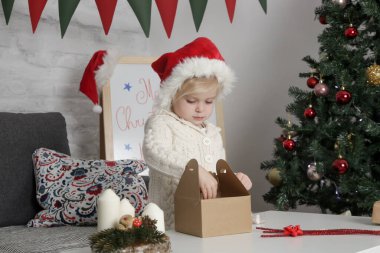 Kırmızı Noel Baba şapkalı sevimli küçük kız evde Noel hediyeleri hazırlıyor.