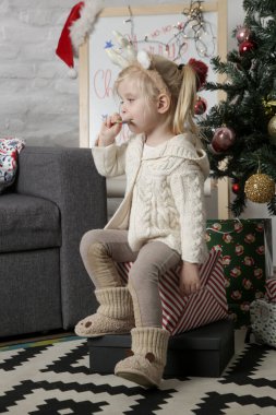 Ren geyiği bandıyla Noel ağacının önünde lolipop yiyen tatlı bir kızın portresi..