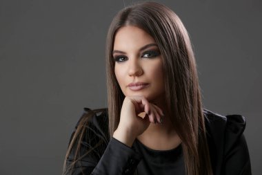 Esmer bir kadının stüdyo portresi. Uzun düz saçları ve göz kamaştırıcı bir makyajı var..