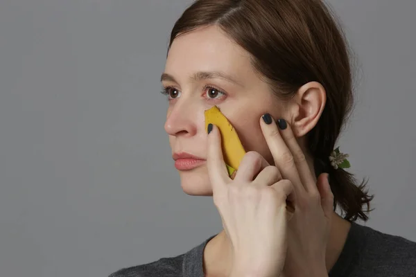 女性は顔にバナナの皮をこすり 肌を明るくし 水和物を減らします 廃棄物ゼロ 天然スキンケアコンセプト — ストック写真