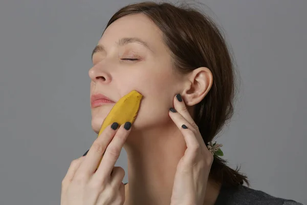 女性は顔にバナナの皮をこすり 肌を明るくし 水和物を減らします 廃棄物ゼロ 天然スキンケアコンセプト — ストック写真