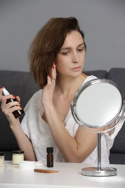 Woman applying hair care spray product on hair ends, split hair tips, dry hair or sun protection concept