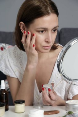 Evde, aynanın önünde cilt bakım ürünleri kullanan bir kadın. Ev hayatı, spa, kişisel bakım ve şımartma konsepti..