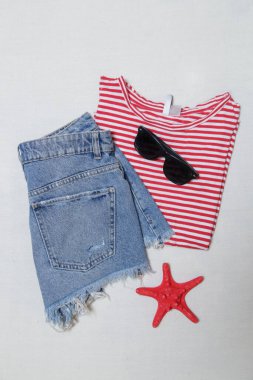 Basit yaz kıyafeti, kot şort ve beyaz arka planda aksesuarları olan çizgili pamuk gömlek. Kadınların günlük moda eşyaları, üst görünüm..