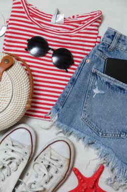 Basit yaz kıyafeti, kot şort ve beyaz arka planda aksesuarları olan çizgili pamuk gömlek. Kadınların günlük moda eşyaları, üst görünüm..