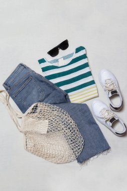 Beyaz arka planda basit bir yaz kıyafeti, çizgili pamuklu gömlek, kot pantolon ve beyaz spor ayakkabılar. Kadınların günlük moda eşyaları, üst görünüm..