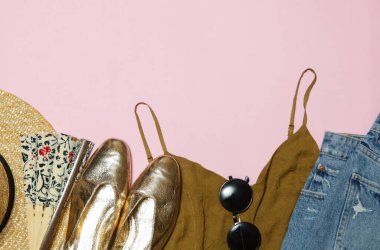Pembe arka planda yaz kıyafeti, kot pantolon, hasır şapka ve altın aksesuarlar. Yaz mevsimi için kadınların moda eşyaları..