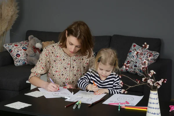 Adorable little girl coloring picture for Easter at home with her mum. Family craft activity with toddlers.