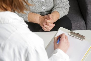 Kıdemli kadın doktoru ziyaret ediyor. Yaşlı hasta ve doktorun not aldığı resmi kapat.