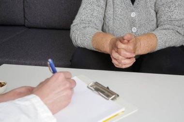 Kıdemli kadın doktoru ziyaret ediyor. Yaşlı hasta ve doktorun not aldığı resmi kapat.