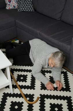 Oturma odasında yerde yatan kıdemli kadın. Kadın kalp krizi, baş dönmesi, baygınlık ya da kaza yüzünden yere düştü. Bastonuyla ayağa kalkmaya çalışan zayıf yaşlı kadın..
