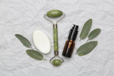 Yüz serumu, yeşim taşı rulo ve beyaz kağıtta sabun. Doğal organik cilt bakım ürünü. Ev spa ve kendine bakım konsepti.