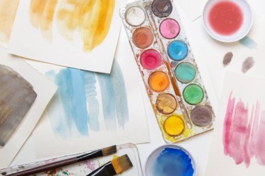 Suluboya palet, fırça ve kağıtları masaya koyar. Yaratıcı hobi ya da sanat terapisi kavramı.