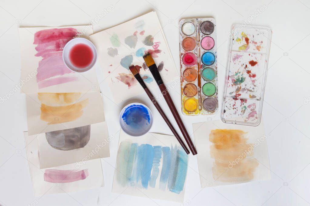 Watercolor paints palette, brushes and papers on table. Creative hobby or art therapy concept.