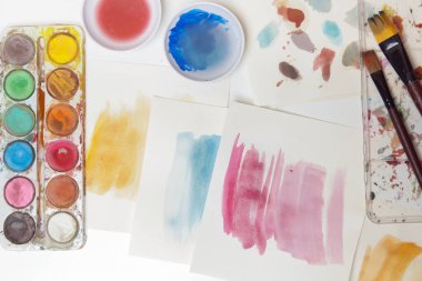 Watercolor paints palette, brushes and papers on table. Creative hobby or art therapy concept. clipart