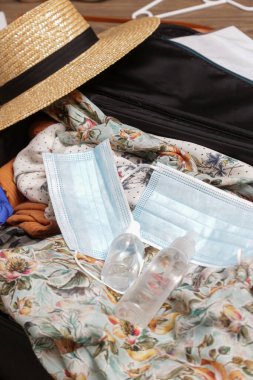 Coronavirus salgını sırasında valiz taşımak için hazırlanıyor. Yüz maskeleri ve el dezenfektanı. Bagajında da yazlık giysiler var. Yeni normal konsept içinde seyahat.