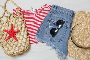 Basit yaz kıyafeti, kot şort ve beyaz arka planda aksesuarları olan çizgili pamuk gömlek. Kadınların günlük moda eşyaları, üst görünüm..