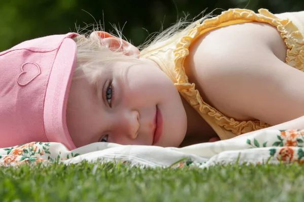 穿着粉色夏帽躺在绿色草地上的可爱小女孩的画像 — 图库照片