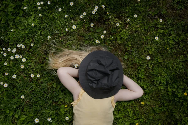 一头长长的金发 蹒跚学步的小女孩躺在绿茵的草地上 头戴帽子 她的户外肖像 — 图库照片