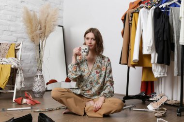 Stresli genç bir kadın darmadağın bir odada kıyafetlerle oturuyor. Giyecek bir şey yok..