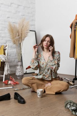 Stresli genç bir kadın darmadağın bir odada kıyafetlerle oturuyor. Giyecek bir şey yok..