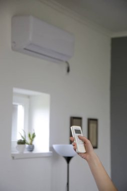 İnsan eli, odadaki sıcaklığı ayarlamak için beyaz klima kumandası kullanıyor..