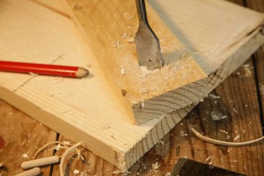 Marangoz atölyedeki tahtaya matkapla delik açıyor.