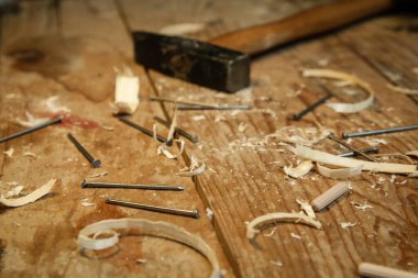 Workshop with tools on the wooden table. Hammer and wooden shavings close up.
