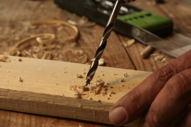 Carpenter using drill machine to make a hole on wooden plank. DIY, woodworking project.