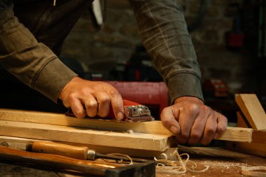 Carpenter planing wood in workshop with a hand planer