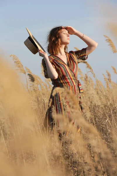 美丽的女人站在草地上 身穿条纹衣服 头戴草帽 休闲夏装 户外肖像画 自然采光 — 图库照片