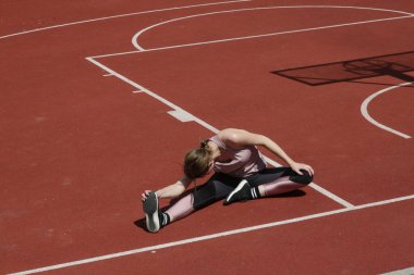 Spor sahasında spor yaptıktan sonra esneme egzersizleri yapan güzel bir kadın fitness modeli.