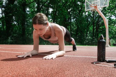 Formda genç bir kadın spor sahasında tahta egzersizi yapıyor. Sporcu kadın dışarıda egzersiz yapıyor..