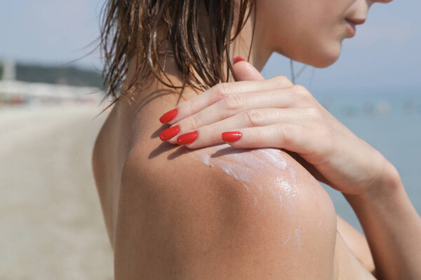 Woman applying sunscreen cream on her shoulder. Sun protection skin care concept.