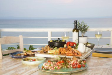 Sebze ve deniz ürünleriyle dolu bir masa. Arka planda deniz ufku var.