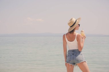 Hasır şapkalı genç bir kadın bir bardak kokteyl tutuyor ve denizin üzerindeki ufka bakıyor. İdilik yaz tatili konsepti.