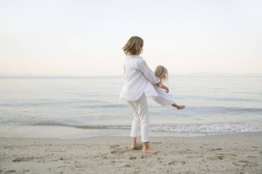 Anne ve kızı sahilde eğleniyor. Anne kızların elini tutuyor ve etrafında dönüyor. Aile aktiviteleri konsepti.
