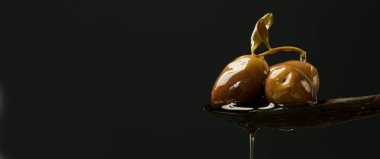 Ekstra bakir zeytinyağı siyah arka planda yeşil zeytinlerle dolu tahta bir kaşıkta akıyor..