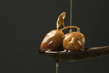 Ekstra bakir zeytinyağı siyah arka planda yeşil zeytinlerle dolu tahta bir kaşıkta akıyor..